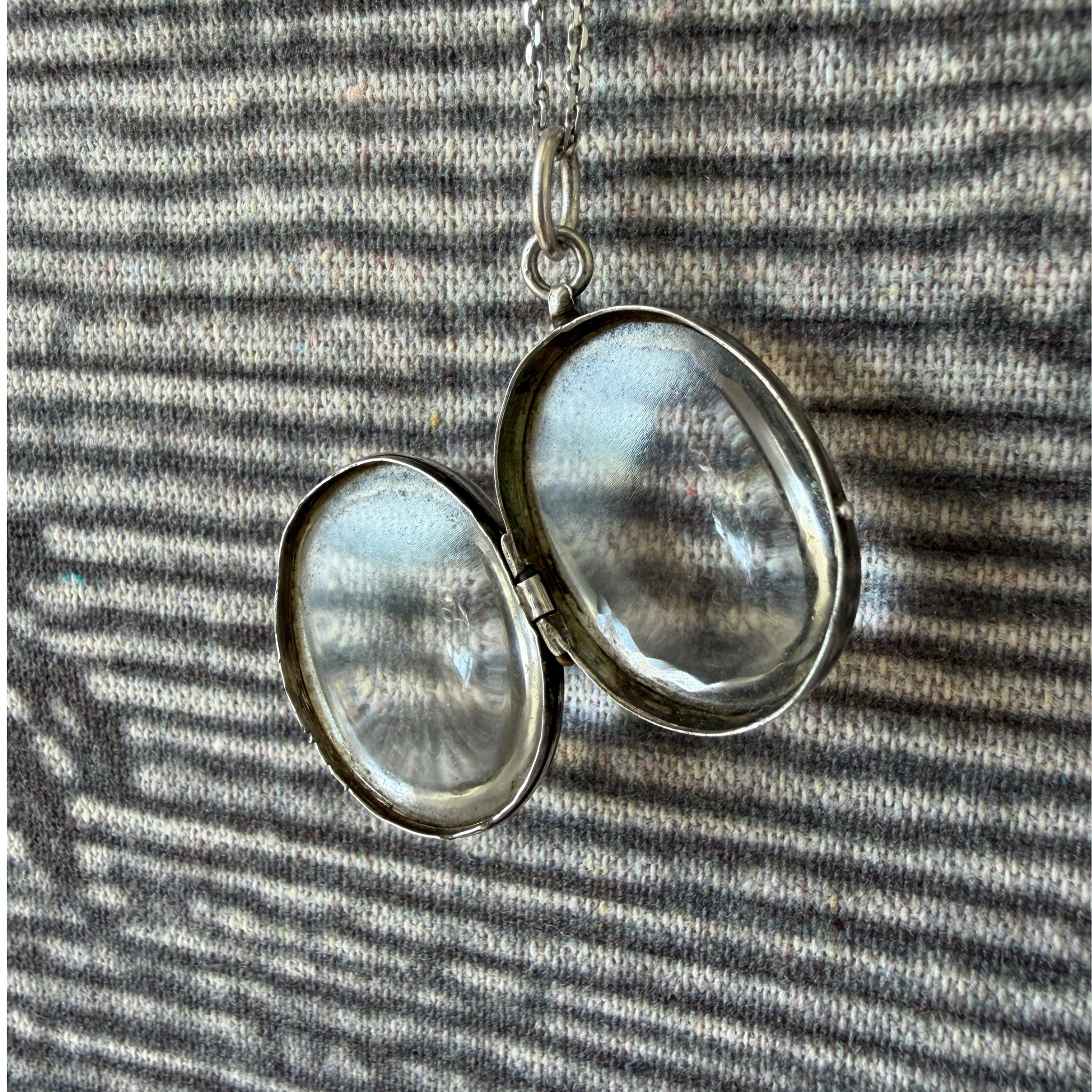Silver locket with two round crystal
panels on a striped fabric background