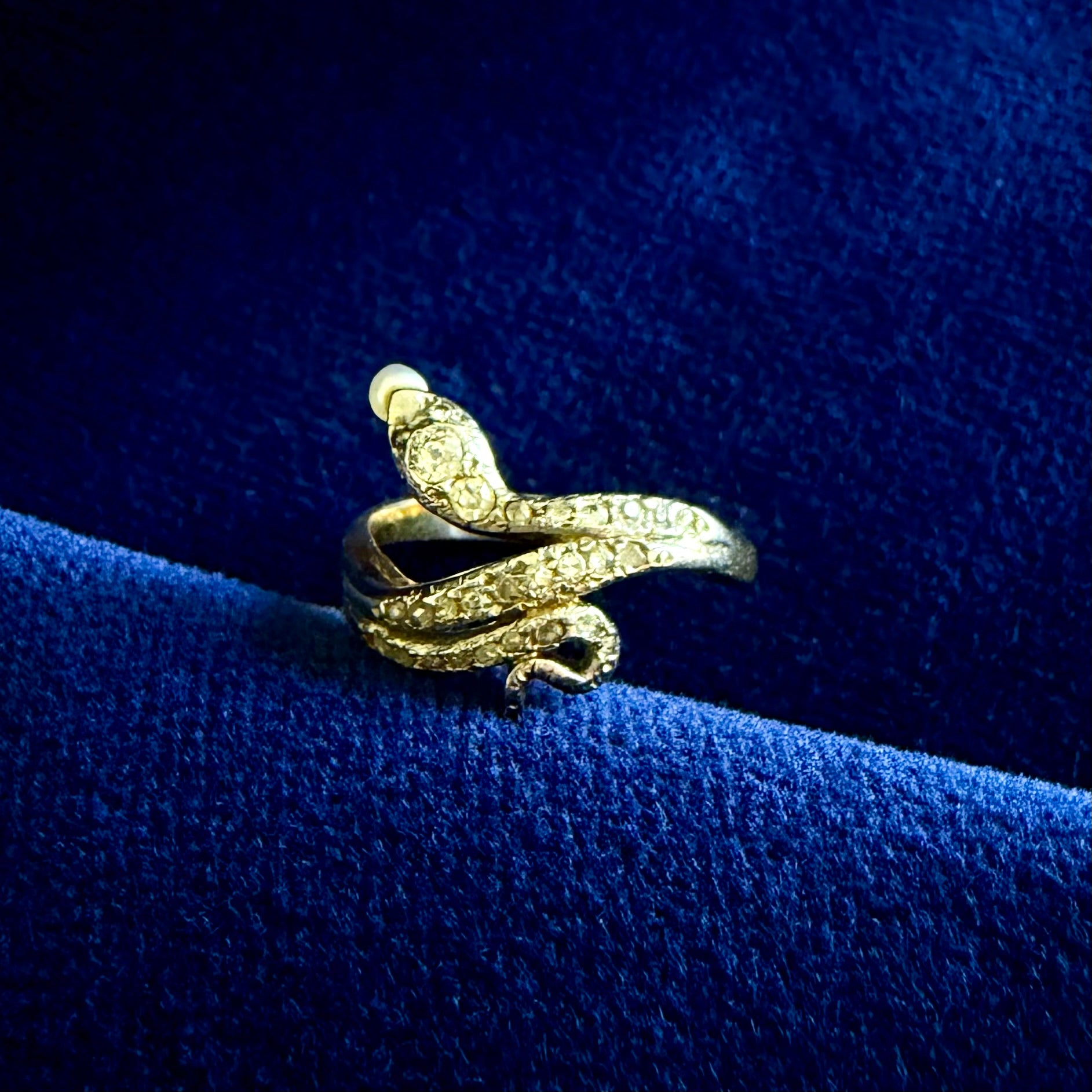 Gold snake-shaped ring on a blue velvet surface