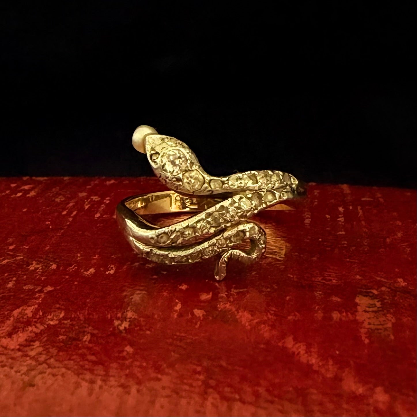Gold snake-shaped ring on a red surface with a black background
