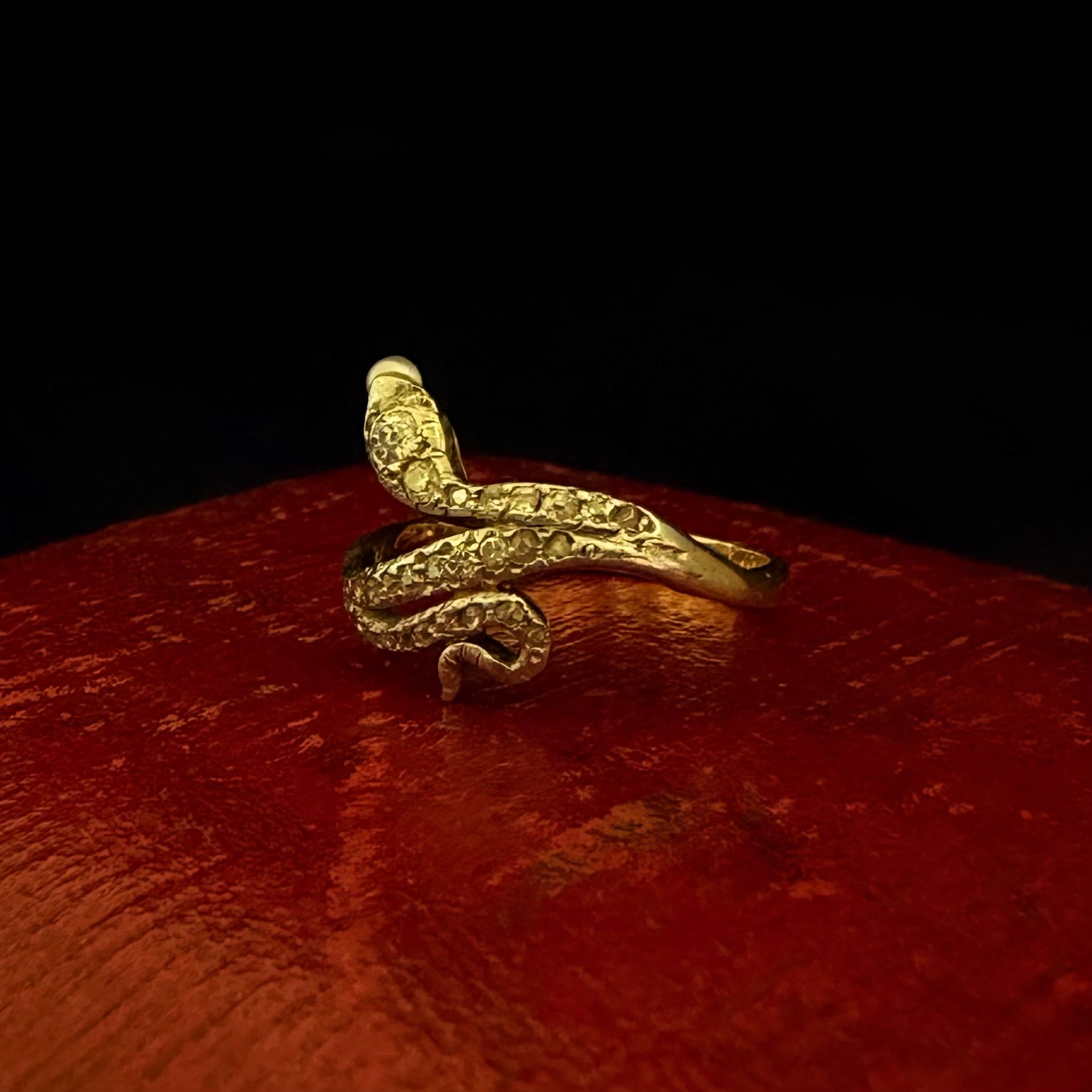 Gold snake-shaped ring on a red surface with a dark background
