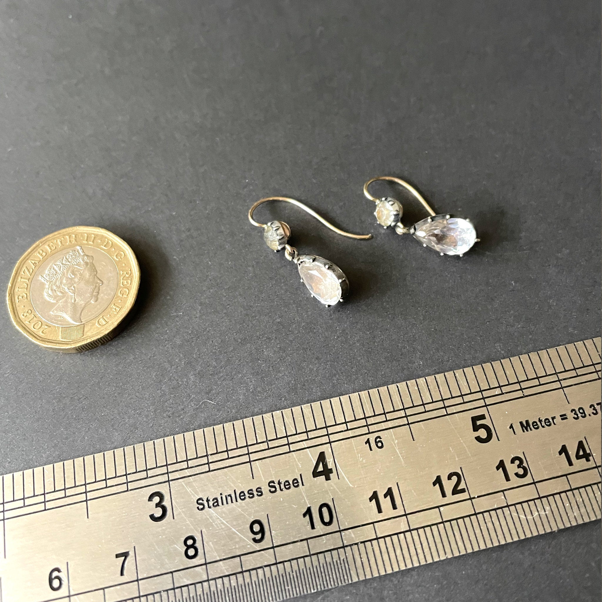 antique earrings next to ruler and pound coin.