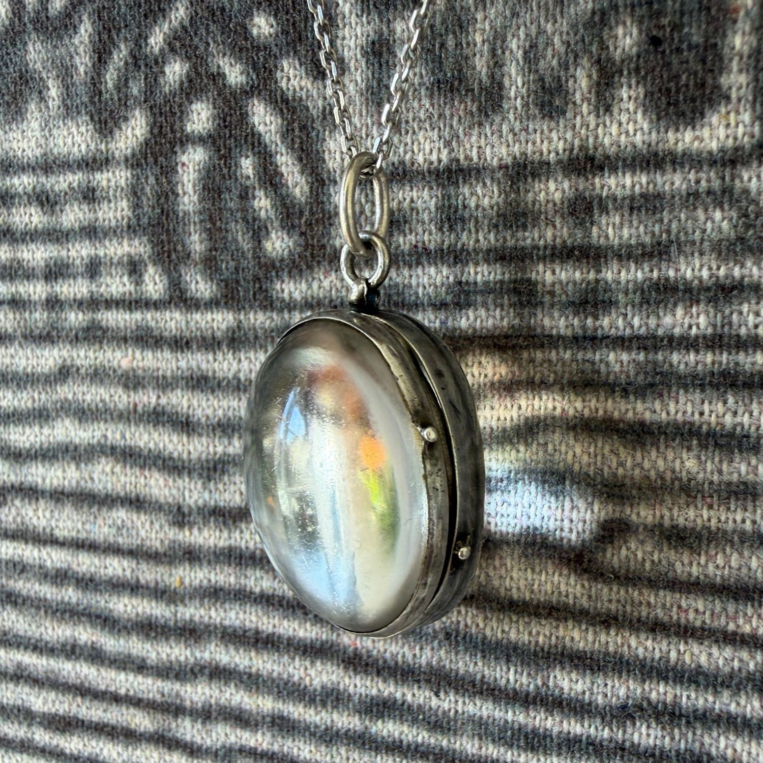 Silver locket with a rainbow-colored stone on a textured fabric background
