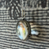Silver locket with a rainbow-colored stone on a textured fabric background