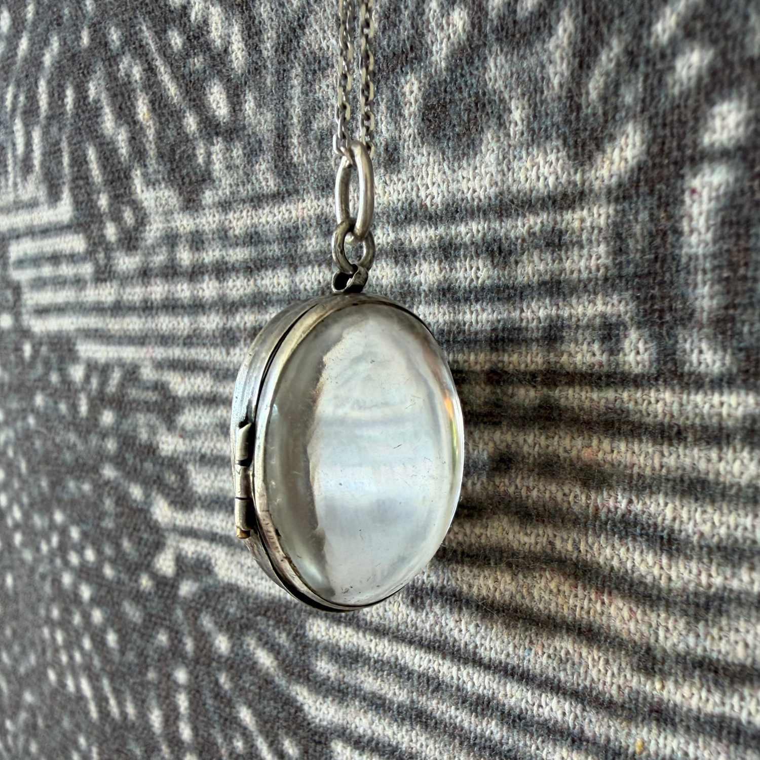 Silver locket with a circular crystal 
design on a textured fabric background