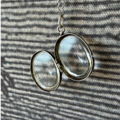 Silver locket with two round crystal 
 panels on a striped fabric background