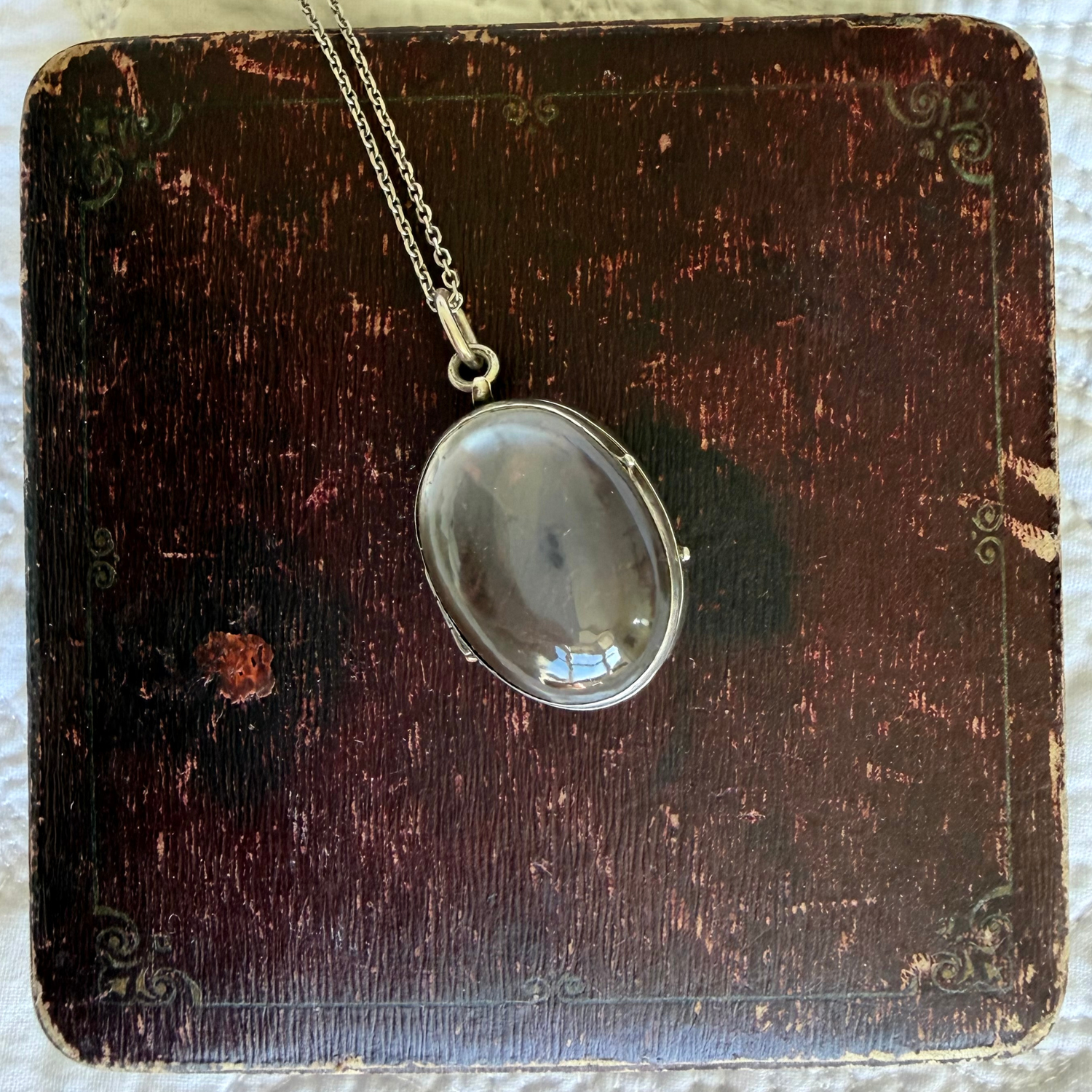 Antique silver locket on a chain against a dark wooden background