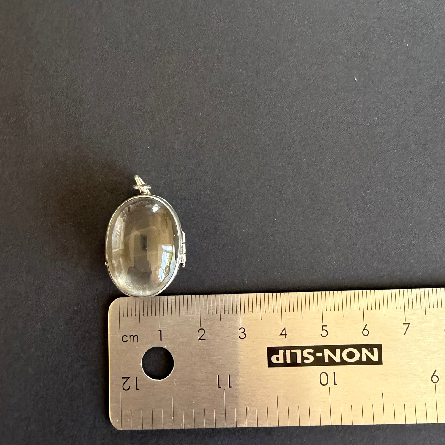 Small oval pendant on a ruler for scale against a dark background