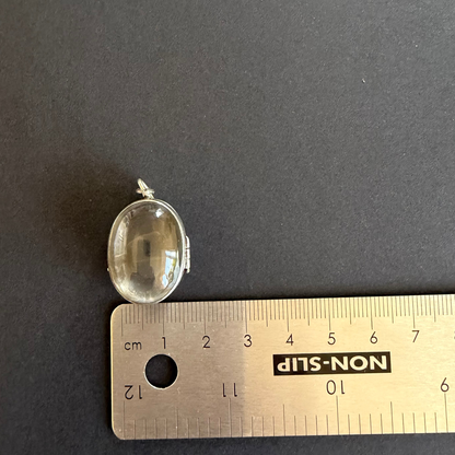 Small oval pendant on a ruler for scale against a dark background