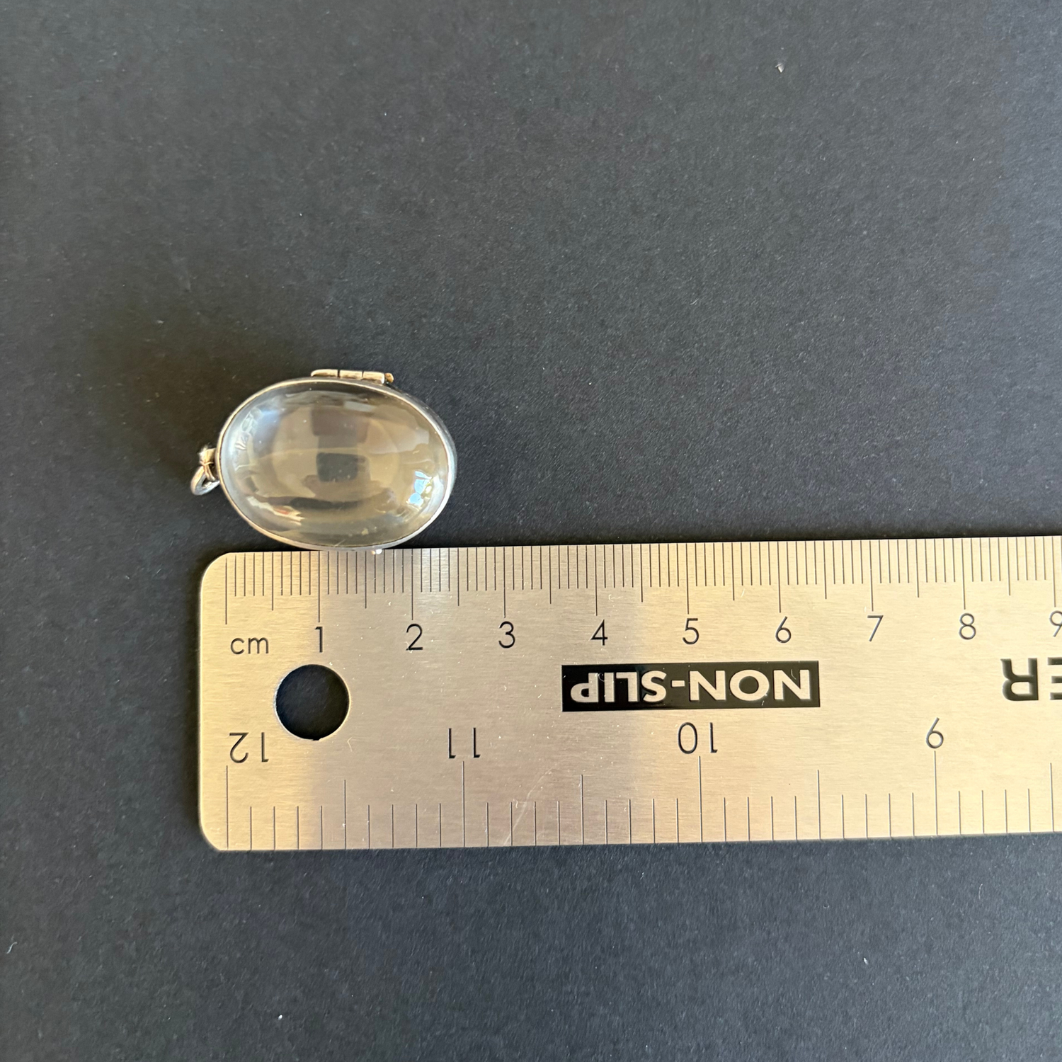 Clear gemstone on a ruler for size reference against a dark background