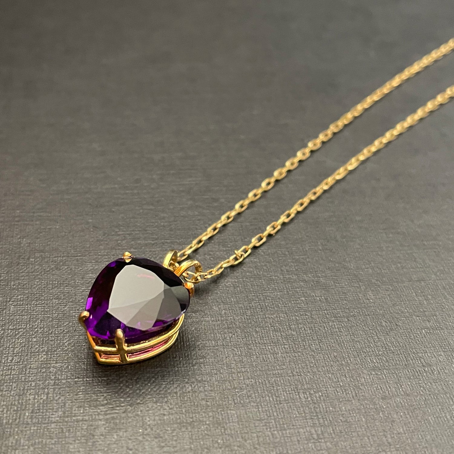 Large heart-shaped amethyst pendant on a gold chain and black background.
