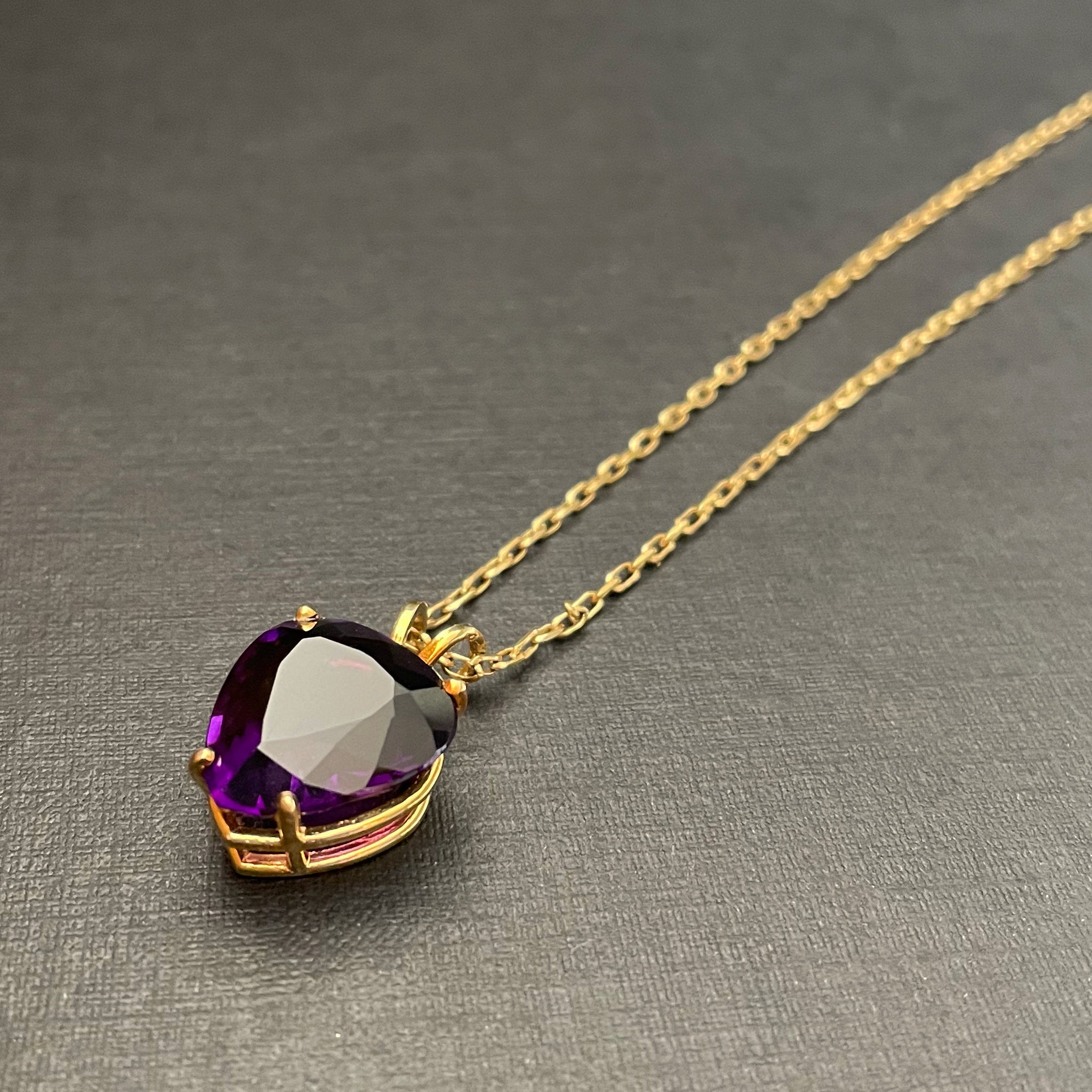 Large heart-shaped amethyst pendant on a gold chain and black background.