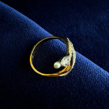 Gold ring with a pearl and small diamond on a dark blue fabric background