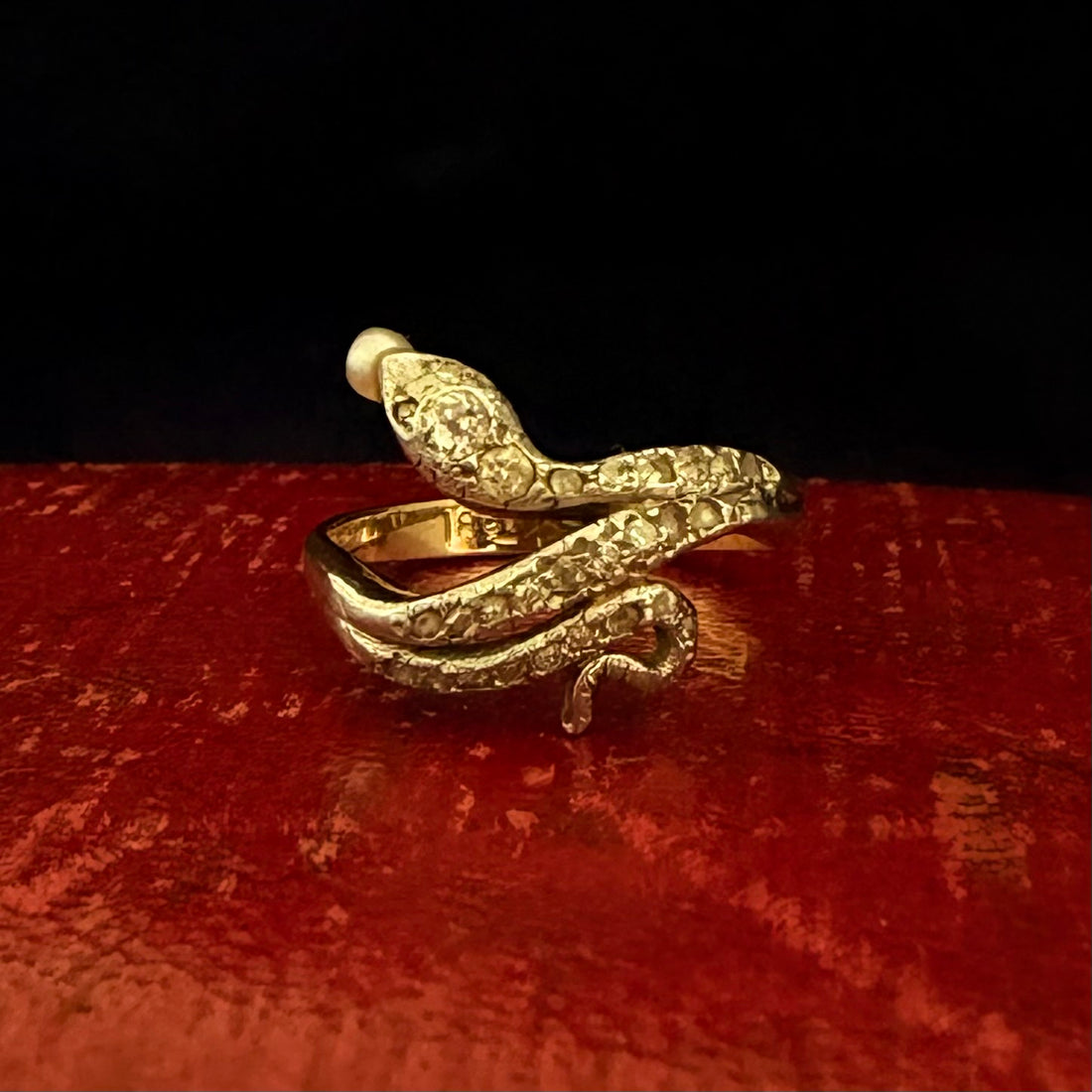 Gold snake-shaped ring on a red surface with a black background