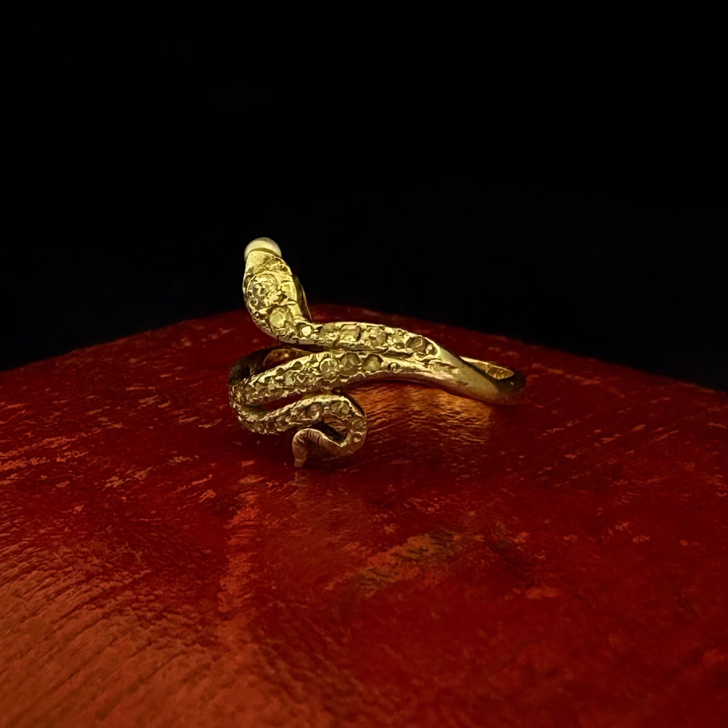 Gold snake-shaped ring on a red surface with a dark background