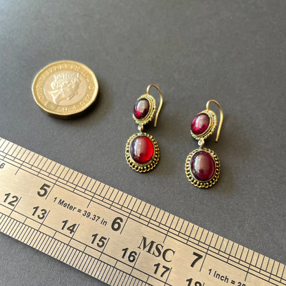 Garnet earrings on black background with gold chain.