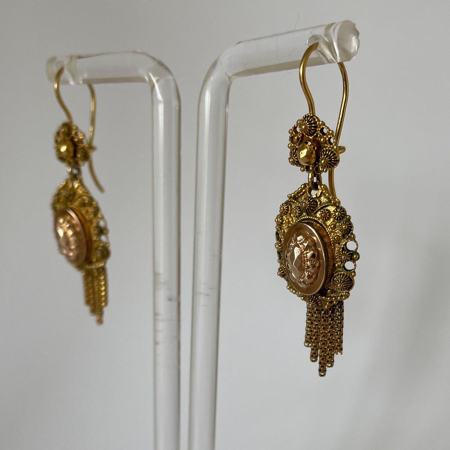 Decorative gold earrings with raised designs and short tassels.