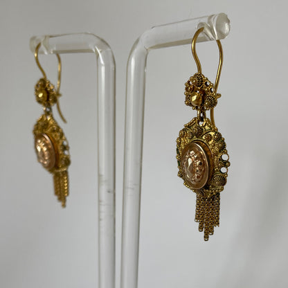 Decorative gold earrings with raised designs and short tassels.
